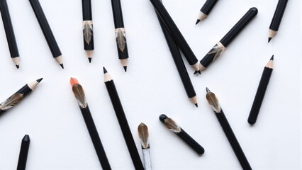 Close-up of multiple used black and beige makeup pencils with some sharpened tips and erasers scattered on a white background, showing various textures and shades