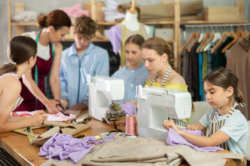 Girl learns to sew on sewing machine in class. Children learn to make a pattern with their teacher