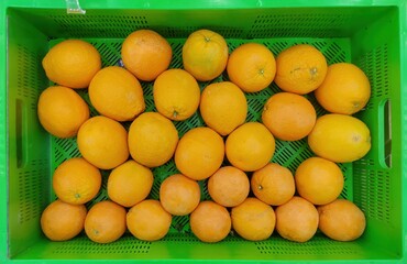 Top view of oranges stacked in a green plastic crate. The texture and grain of the fruit is clearly...