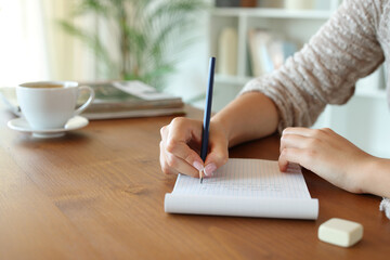 Woman hand writing on paper notebook on wooden table