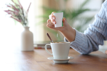 Woman hand throwing saccharin pill on coffee cup at home