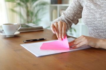 Woman hand removing sticky note from paper at home