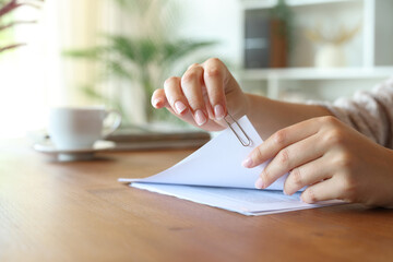 Woman hand putting a paper clip on document sheets at home