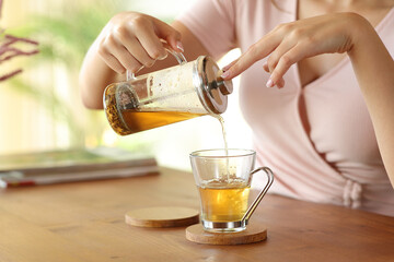 Woman hand pouring tea on glass at home