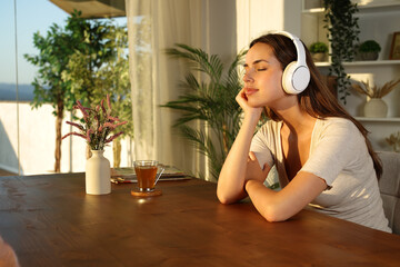 Woman relaxing listening audio with headphone at sunset at home