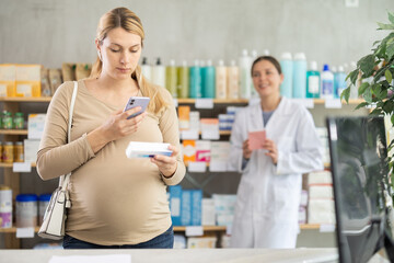 Pregnant woman scanning qr code for box of pills with woman pharmacist in pharmacy