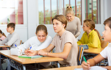 Group of diligent school kids and teacher during lesson in classroom in secondary school