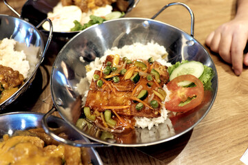 Pan-fried dish with a flavorful sauce, featuring tofu-like pieces and mixed vegetables over rice, served in a sizzling pan. Pan-fried dish with a flavorful sauce, featuring tofu-like pieces and mixed 
