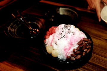 Shaved ice dessert with red beans, lychee, and syrup, topped with chia seeds, offering a refreshing...