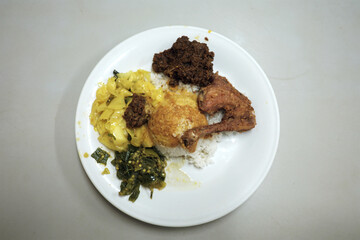 A delicious Nasi Padang plate featuring rice with gulai sauce, gulai cabbage, fried chicken drumstick, flavorful beef rendang, and spicy green chili sambal.
