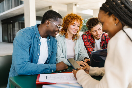 University students sitting around a table studying together happy and tyiping on the laptop and mobile phone