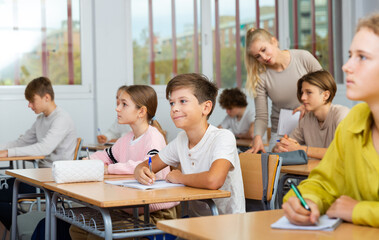 Fototapeta premium Smiling american school boy sitting at the desk in classroom at lesson in secondary school