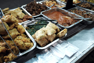 The layout displays numerous metal trays filled with a wide array of prepared dishes, suggesting a 