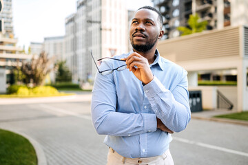 Businessman reflecting in a modern urban setting while holding glasses outdoors in the late...