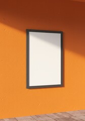 Photo of a blank framed poster hangs on an orange textured wall with sunlight