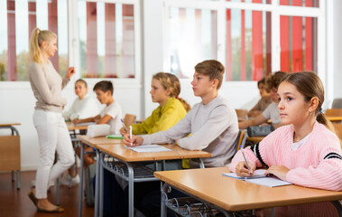 Fototapeta premium Teenagers sitting at desks in classroom during lesson and doing tasks.