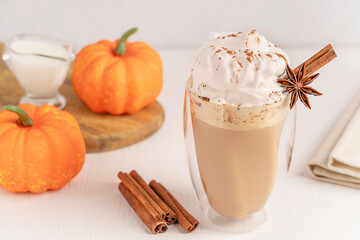 Sweet morning pumpkin spice latte made from coffee and milk with whipped cream topping and cinnamon and anise garnish served in drinking glass on white wooden table table for autumn breakfast drink