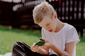 A boy with hearing aids gazes curiously at a snail on a leaf, capturing a magical childhood moment...