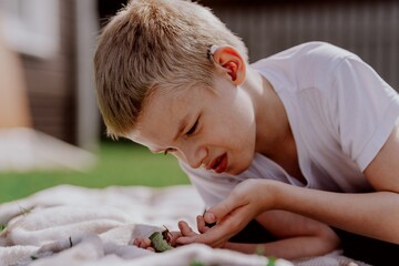 A boy with hearing aids gazes curiously at a snail on a leaf, capturing a magical childhood moment...