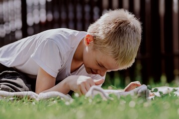 A boy with hearing aids plays on the grass while engaging with gadgets - drawing on a tablet and...