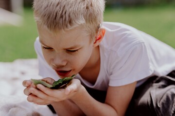 A boy with hearing aids gazes curiously at a snail on a leaf, capturing a magical childhood moment...