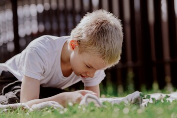 A boy with hearing aids plays on the grass while engaging with gadgets - drawing on a tablet and...
