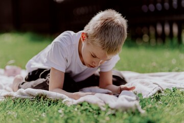A boy with hearing aids plays on the grass while engaging with gadgets - drawing on a tablet and...