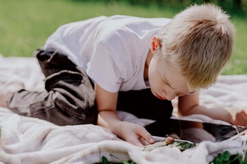 A boy with hearing aids gazes curiously at a snail on a leaf, capturing a magical childhood moment...