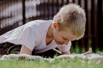 A boy with hearing aids plays on the grass while engaging with gadgets - drawing on a tablet and...