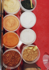 Vibrant seasoning powders on a red stall surface. While enhancing fried snacks, these are high in sodium & MSG, offering little nutrition. Excessive use can lead to an imbalanced diet.