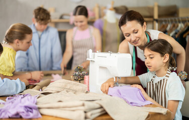 Little enthusiastic girl, about eight, concentrating on sewing in cozy school tailoring workshop,...