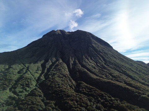 Sunrise photo from Mount Apo&rsquo;s foot shows its ridged emerald cone towering under a soft blue dawn sky, early light tracing lush volcanic slopes on Mindanao.