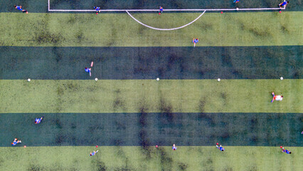Top-down aerial view of children training and playing football on a striped green artificial turf soccer field.