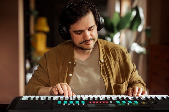 Man playing synthesizer at home with headphones