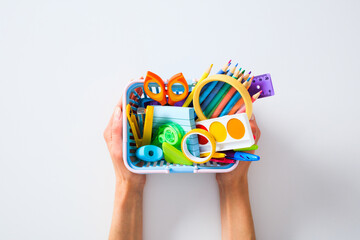 School supplies in basket held by hands on white background