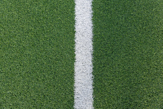 Top view of artificial football field with a white center line. Vivid green turf and clean dividing stripe. Sports field symmetry and design