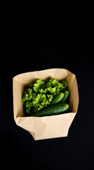 Fresh green vegetables including broccoli, cucumber, and leafy greens in a brown paper bag on a black background, showcasing healthy produce and natural textures for a vibrant, nutritious display