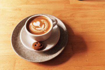 A perfectly crafted latte with heart-shaped latte art, served with a small cookie on a rustic plate, inviting a moment of calm.