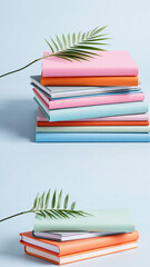 Stacked colorful notebooks with pastel covers and green palm leaves on a light blue background, creating a fresh and organized aesthetic