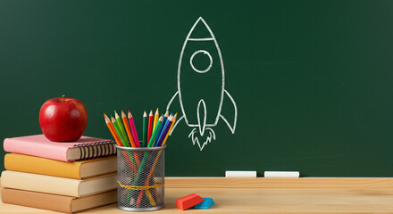 Colorful Pencils, Books, and Apple by Green Chalkboard with Rocket Drawing, Educational Supplies for Students and Teachers - back to school