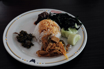 A classic Nasi Padang plate with rice, gulai curry, cassava leaves, young jackfruit gulai, cucumber, green chili, and beef rendang.