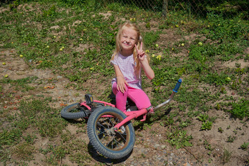 A bicycle is lying on the ground, and a little girl is sitting on it, A little girl is sitting on...