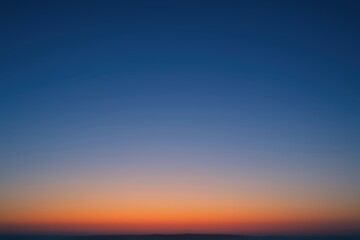 Fototapeta premium Vibrant orange and pink sunset sky gradient over a distant dark horizon