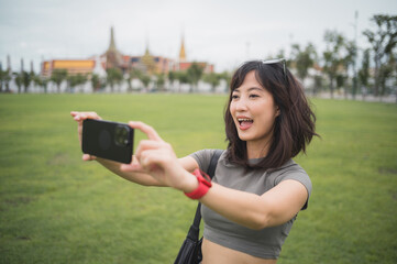 Happy southeast asian woman teenager blogger on solo world travel take photo with smartphone. Local...