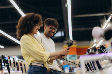 Smiling Couple Testing Hairdryers in Modern Electronics Store