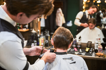 Back view of professional hairdresser making stylish haircut. Barber in fancy outfit using a comb...