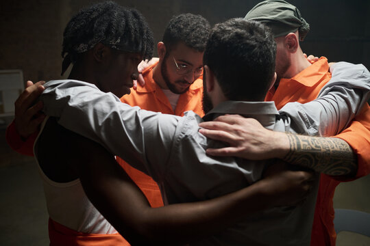 Group of young multiethnic men standing in close circle embracing each other during group therapy session in prison setting showing support and unity