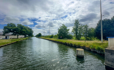 A serene and peaceful canal scene featuring lush green trees along with a dramatic sky, ideal for nature enthusiasts