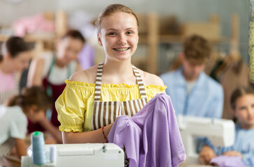 Teen girl student of school of young fashion designers carefully examines fabric, evaluates product...