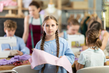 Portrait of a happy girl with a pattern and fabric in her hands during a sewing lesson